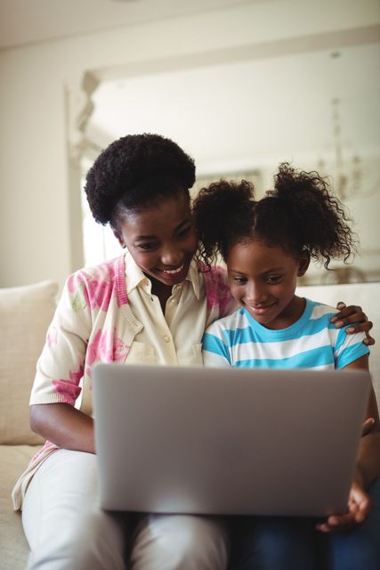 Smiling mother and daughter using laptop in living room at home