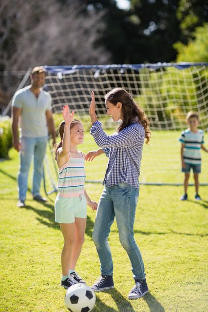 Happy mother and daughter giving high five while playing football in park