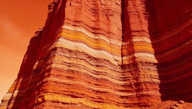 Towering banded sandstone cliff showing striking red orange yellow layered rock strata