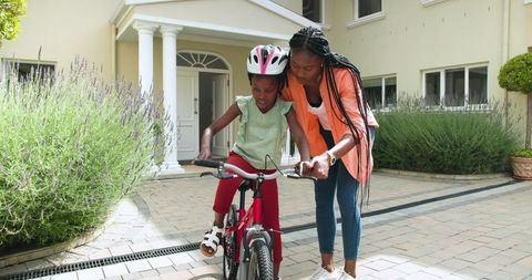 Mother Teaching Daughter to Ride Bicycle Outside Home