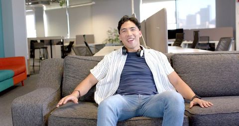 Young man relaxing on office lounge sofa with headphones smiling in modern coworking space