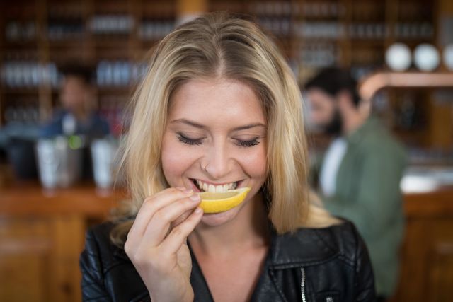 Beautiful woman biting into lemon wedge after having tequila shot in bar