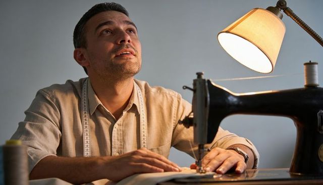 Tailor sewing at vintage sewing machine with lamp and measuring tape, focused craftsmanship