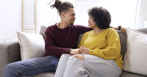 Couple relaxing on couch holding hands wearing knit sweaters in bright cozy living room