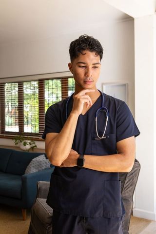 Contemplative male healthcare worker in navy scrubs at home