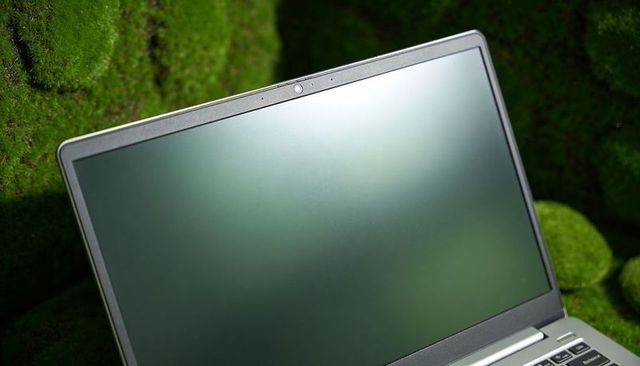 Minimalist laptop featuring matte screen and centered webcam resting on green moss backdrop