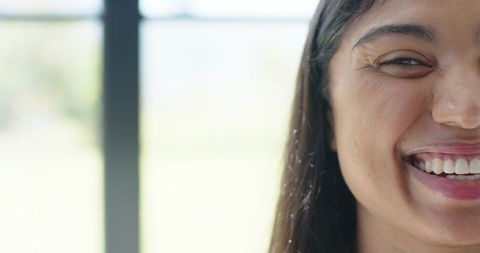Smiling woman crinkling eye near sunlit window with soft rimlight and bokeh background