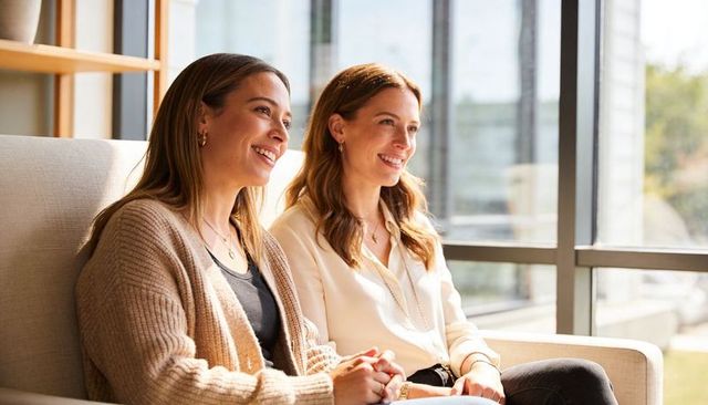 Two women sharing warm conversation on lounge sofa by sunlit window, casual meeting