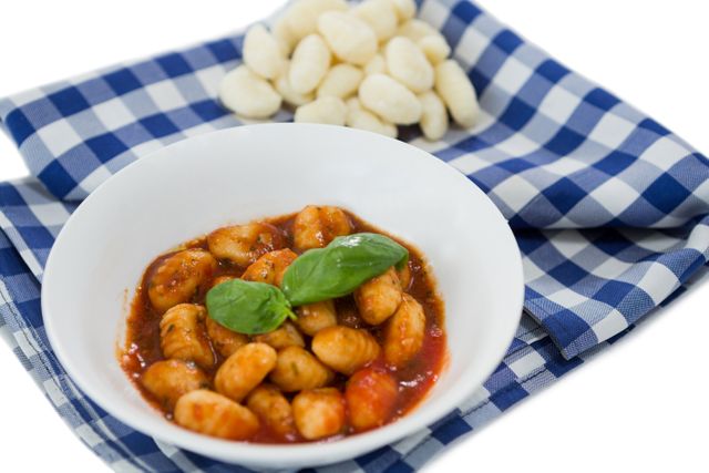 Close up of gnocchi pasta in bowl on napkin against white background