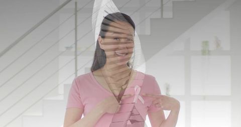 Smiling woman wearing pink top pointing to pink ribbon promoting breast cancer awareness