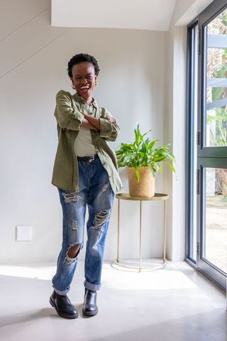 African american woman standing in bright modern interior wearing olive shirt and distressed jeans