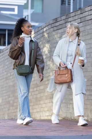 Diverse women walking and chatting with coffee beside curved brick wall urban style