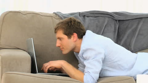 Man Relaxing on Couch Working on Laptop Enthusiastically