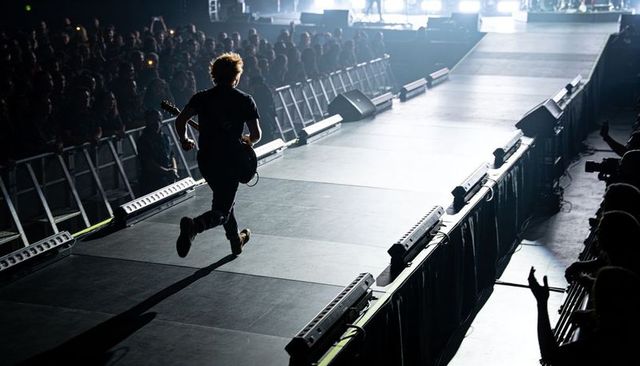 Backlit guitarist sprinting down arena runway silhouette conveying high-energy live concert