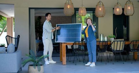 Couple holding solar panel on patio promoting sustainable home energy and outdoor living