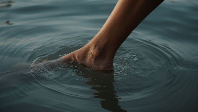 Bare foot dipping into teal lake water creating concentric ripples and soft reflection