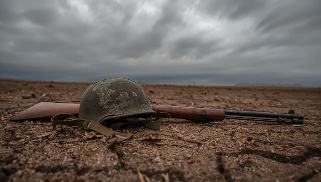 Vintage military helmet and rifle on desolate battlefield