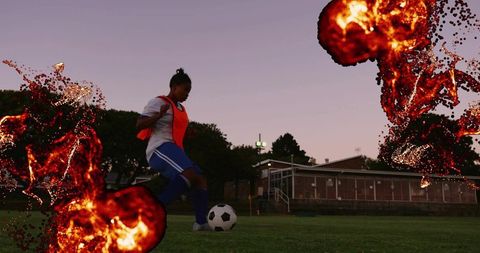 Teen soccer player dribbling ball wearing orange bib on grass field under lights at dusk