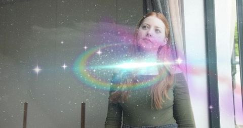 Redhead woman standing and gazing through glass door with dreamy rainbow flare