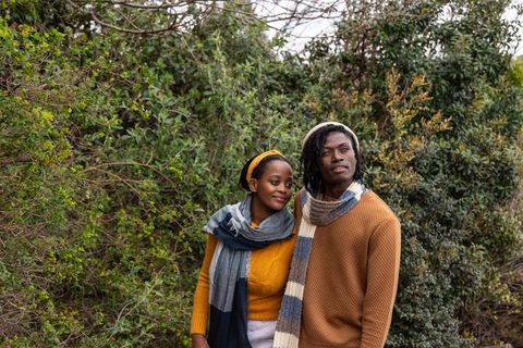 African american couple standing close in park wearing knit scarves and autumn sweaters