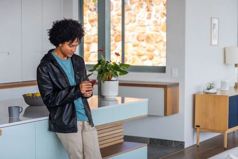 Young african american man leaning on modern kitchen island holding smartphone in leather jacket