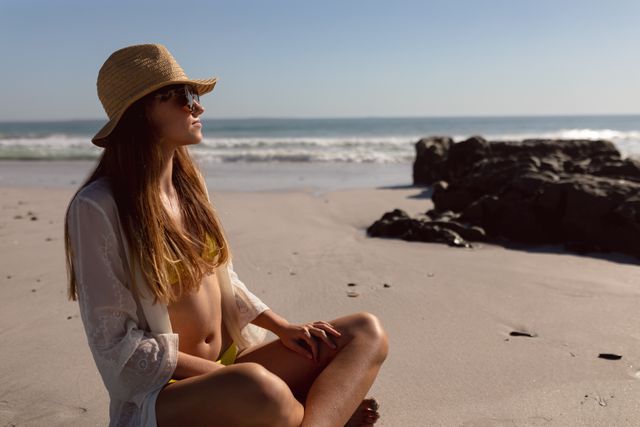 Beautiful woman in sunglasses and hat relaxing on the beach