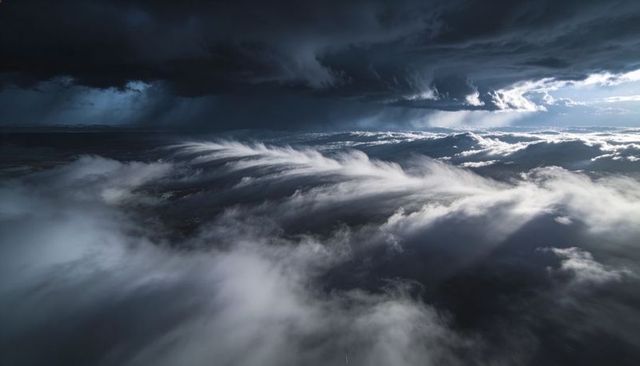 Sunbeams piercing dramatic rolling storm clouds over layered mist conveying depth
