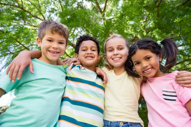Group of happy children standing close together under a tree, smiling and enjoying their time outdoors. Perfect for use in advertisements, educational materials, and websites promoting children's activities, friendship, and outdoor play.