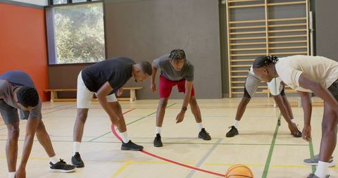 African american male basketball team stretching together on gym court before practice