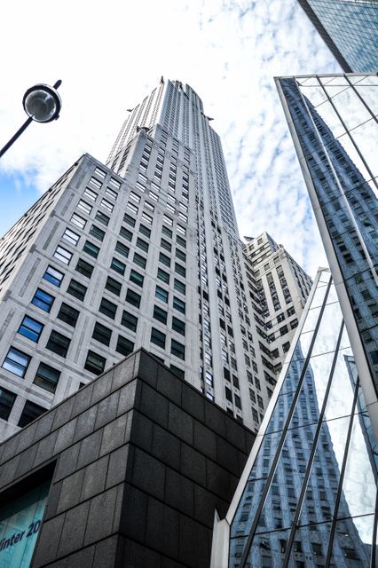 Image depicts a dynamic view of urban skyscrapers from a low angle, highlighting modern architecture and glass reflections. This can be used in business or real estate marketing materials, presentations, or articles about urban development, architecture, and city life.