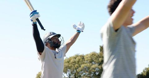 Cricket batsman celebrating and appealing with raised bat and helmet on sunny outfield