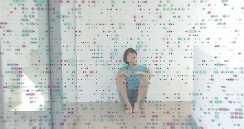 Solitary young man sitting on floor behind dotted glass panel in minimalist interior