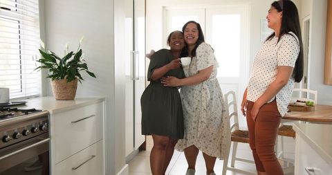 Cheerful women celebrating friendship and pregnancy announcement in bright kitchen