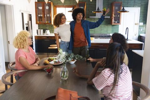 Diverse friends gathering around dining table sharing cheese platter in openplan kitchen