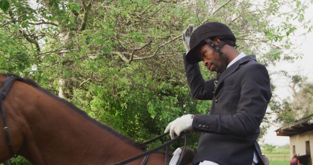 Pensive african american man in riding clothes sitting on horse and adjusting riding hat - Download Free Stock Photos Pikwizard.com