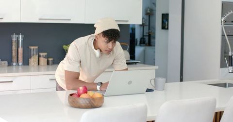 Young man leaning over laptop on modern kitchen island for remote work and morning coffee