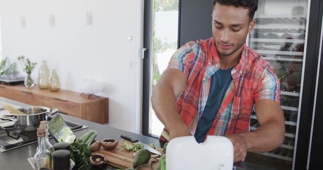 Man preparing a fresh meal in a modern kitchen, chopping vegetables and using appliances. Suitable for content related to cooking, healthy eating, domestic life, kitchen appliances, meal preparation, and lifestyle blogs.