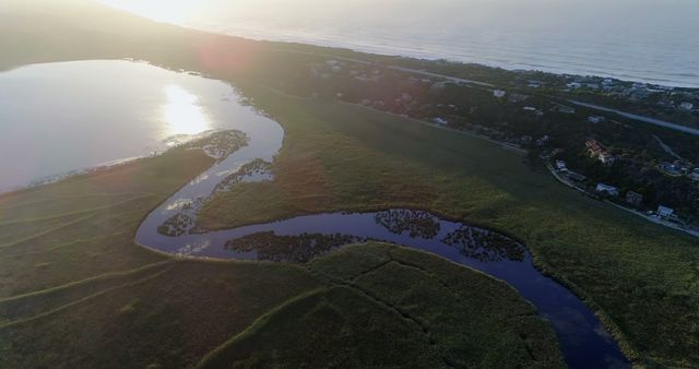 This image captures a stunning aerial view of a coastal marshland during sunset, featuring a winding river and lush greenery. Ideal for use in nature-themed projects, travel blogs, environmental articles, and regional promotional materials. The tranquil and beautiful scenery highlights the serene beauty of nature, which works well for relaxation and wellness campaigns.