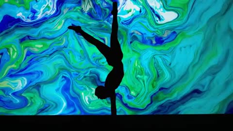 Silhouette Acrobat Performing Handstand Pole Routine Against Swirling Marble LED Projection