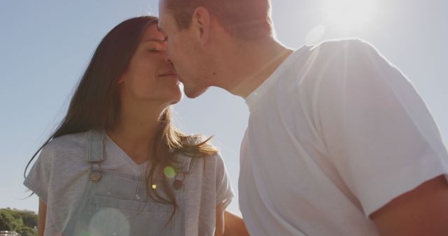 Capturing a tender moment of a couple sharing a kiss under bright sunlight. Perfect for use in marketing materials related to romance, happiness, and outdoor activities. Can be used for social media campaigns, blogs about relationships, or as a cover image for romantic content.