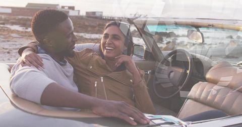 Smiling couple enjoying convertible road trip along rocky coast at golden hour
