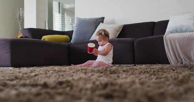 Caucasian baby playing with a plastic cup while sitting on the floor at home - Download Free Stock Photos Pikwizard.com