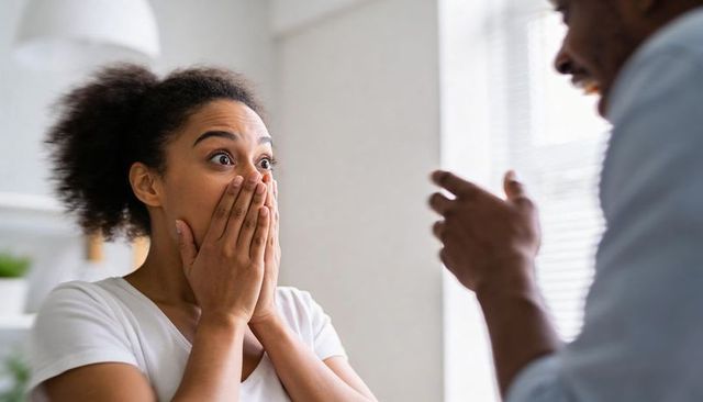Surprised woman covering mouth reacting to joyful surprise from partner in bright room