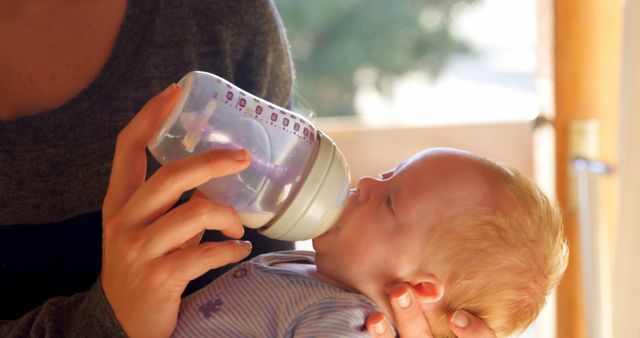 A Caucasian baby is being fed from a bottle by an adult, with copy space. Capturing a nurturing moment, the image reflects the care and feeding routine of an infant.
