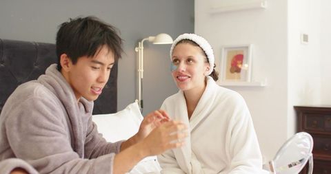 Couple enjoying cozy at-home skincare ritual in robes on bed, intimate morning routine