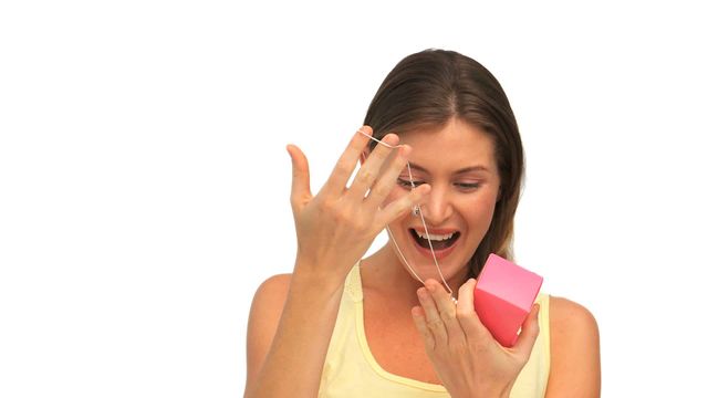 A woman dressed in a casual yellow top is smiling excitedly while opening a gift box. The small pink box contains a piece of jewelry, bringing a look of surprise and happiness to her face. This stock photo is ideal for marketing related to gifting, jewelry promotions, holiday celebrations, engagements, and lifestyle blogs focusing on joyful moments and personal experiences.