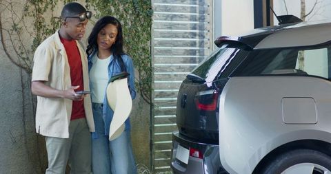 Couple examining electric hatchback and discussing via smartphone