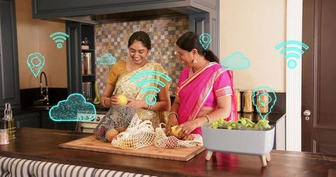Women preparing fruit on modern kitchen island wearing sarees with smart home icons