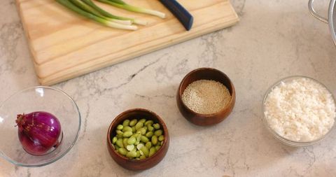 Top-down prep for sushi bowl with rice, edamame, sesame seeds, red onion and scallions