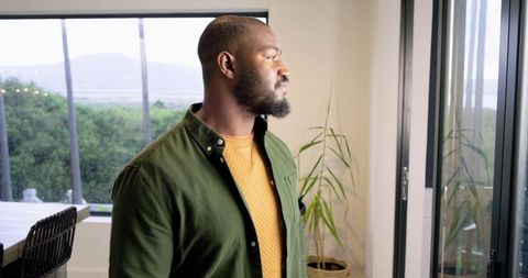 Mid adult African American man standing and looking out sliding glass door in home